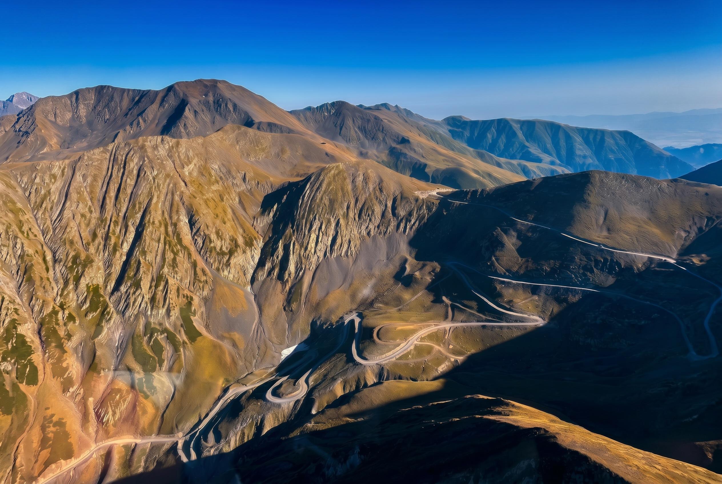 Aerial view of winding mountain roads crossing steep, rocky slopes under a clear blue sky in Georgia's Kakheti region, famed for its wine.