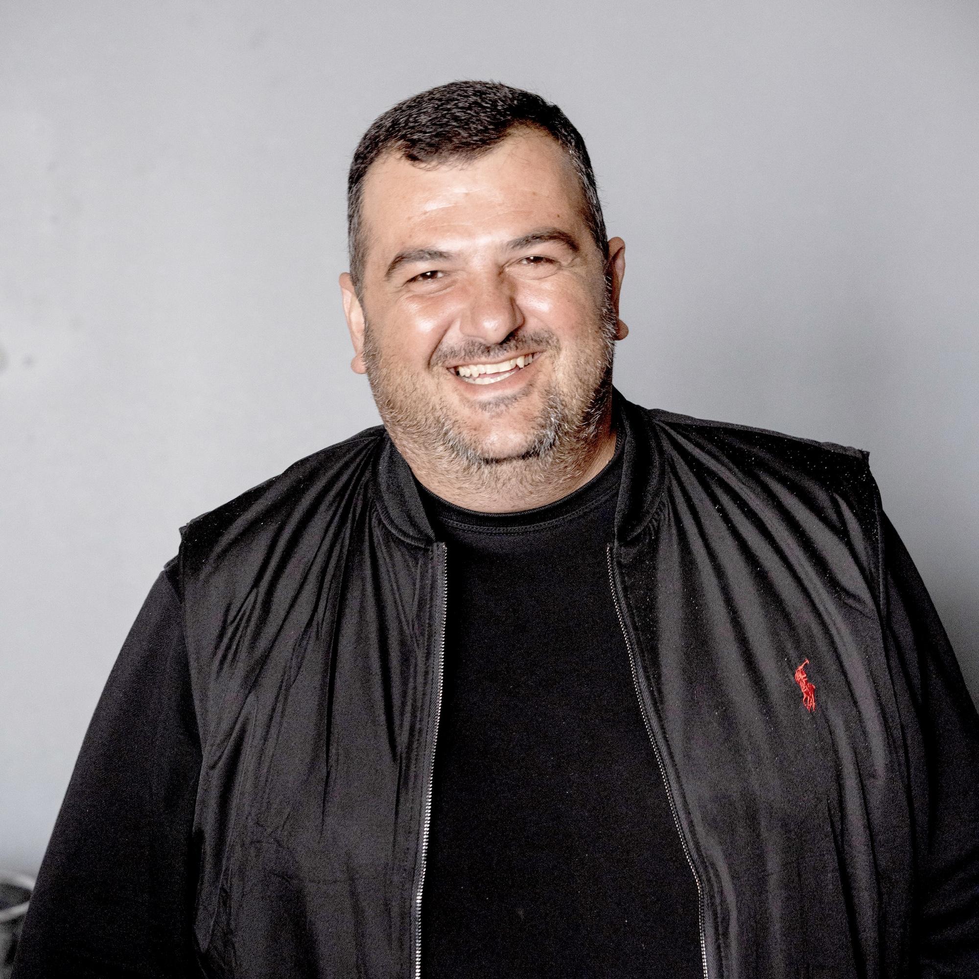 Levan smiling, wearing a black shirt and black vest.