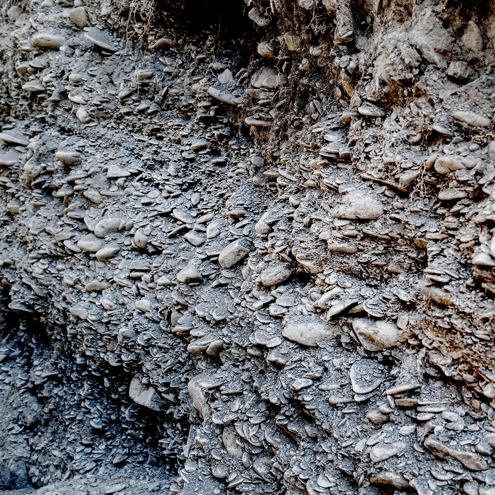 A close-up view of a rock face with layers of embedded stones, showing various sizes and shapes tightly packed together in horizontal strata.